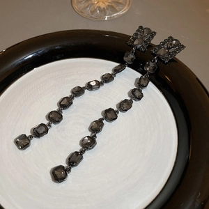 Close-up of elegant long drop earrings with dark grey gemstones on a ceramic plate