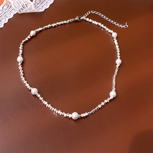 Détail macro de perles argentées et perles blanches sur le collier à fermoir mousqueton