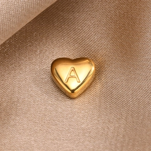 Polished gold heart charm pendant with engraved letter A on a silk fabric background