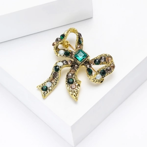 Close-up of golden bow brooch with green square gemstone and colorful rhinestones