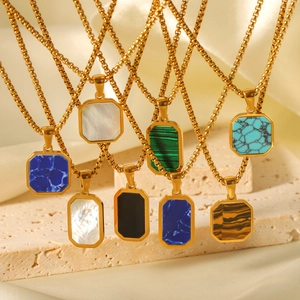 Close-up of gold necklaces with colorful octagonal gemstone pendants on a stone base
