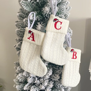 Detail of three white knitted Christmas stockings with red embroidered letters A, B, and C