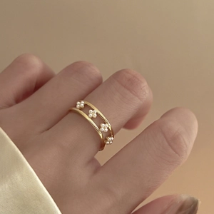 Detail view of double-layered gold ring with elegant pearl floral motifs on female hand