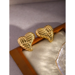 Macro shot of 18k gold heart earrings with textured horizontal stripes on dark wood