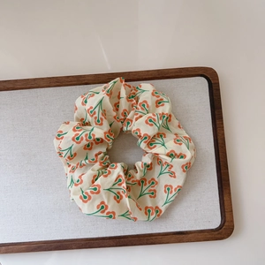 Close-up of a floral cotton scrunchie with orange blossom pattern on linen background
