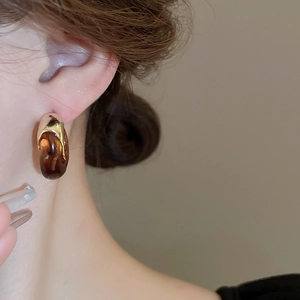 Close-up of amber resin C-shape earring with gold metallic accent on model's ear