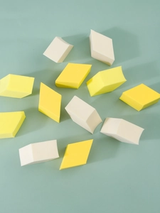 Macro shot of diamond-shaped makeup sponges in yellow and cream on mint background
