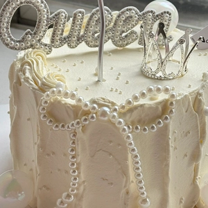 Detailed view of silver Queen cake topper with pearls, rhinestones, and mini crown
