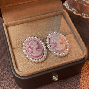Macro shot of vintage pink cameo lady earrings with faux pearl border on velvet