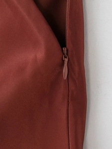 Detailed view of the invisible side zipper on a reddish-brown satin textured skirt