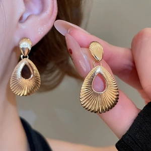 Close-up of golden teardrop hollow earrings with elegant sunburst texture detail
