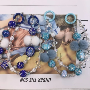 Detailed view of blue beaded phone charms with faux fur pom poms and rhinestone balls