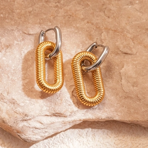 Macro detail of 18k gold plated textured link earrings on a beige stone surface