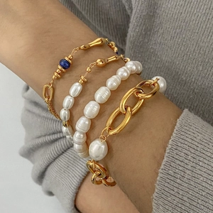 Layered gold chain bracelets with baroque pearls and blue gemstone on female wrist