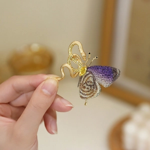 Detailed view of a gold snake and butterfly brooch with purple wings and a yellow gem