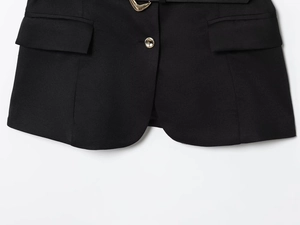 Detail of black sleeveless vest featuring gold buttons, fabric texture and belt buckle