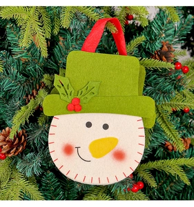 Close-up of a snowman felt gift bag hanging on a Christmas tree with pine cones and berries
