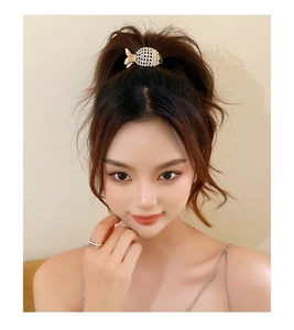 Détail d'une pince à cheveux dorée en forme de poisson avec perles et strass