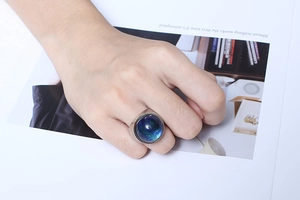 Detail of a large round ring featuring blue and green gradient foil glass on a female finger