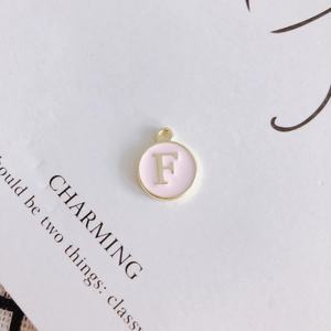Detailed view of round pink enamel pendant with gold letter F for DIY jewelry making