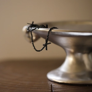 Detailed shot of black spinel bead necklace with small cross pendants on silver bowl