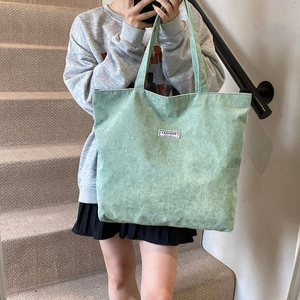 Detailed texture of thick corduroy tote bag in light green with woven brand label