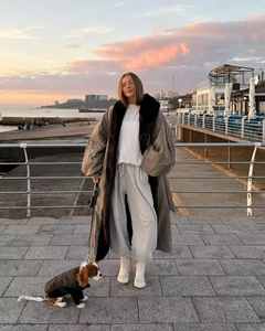 Piumino lungo grigio-marrone invernale oversize con collo in pelliccia sulla spiaggia al tramonto