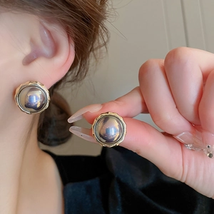 Gros plan sur boucles d'oreilles dorées avec perle irisée centrale et bordure texturée