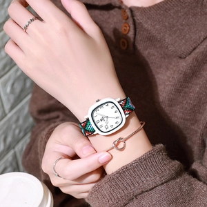 Detail shot of a square quartz watch featuring a colorful woven fabric strap on a wrist