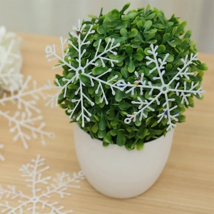 Close-up of white glitter snowflake ornaments on green plant and wooden surface