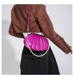Detail der muschelförmigen lila Handtasche mit Perlengriff und glänzendem Finish