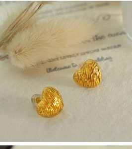 Macro detail of gold woven heart earrings with vintage texture on a soft floral background