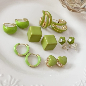 Detailed view of green enamel heart and geometric stud earrings set on a white ceramic plate