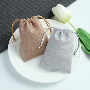 Sparkling gold and silver drawstring jewelry gift pouches displayed on a white ceramic plate