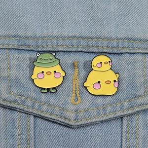 Close-up of cute yellow chick enamel pins with green frog hat on denim jacket pocket
