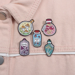 Detail of five mushroom magic potion enamel pins on pink denim fabric background