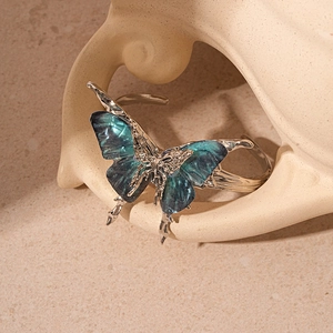 Macro detail of silver-tone open cuff bracelet with gradient blue-green resin butterfly