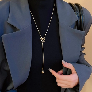 Detail of a minimalist gold Y-necklace with an OT buckle and ball pendant on a model