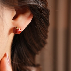 Close-up of a model wearing vintage red apple studs with golden leaves on warm background