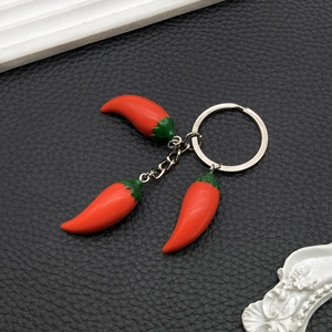 Detail of three red resin chili pepper pendants on a metal keychain over leather