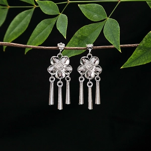 Detailed view of silver flower tassel earrings hanging on a green leaf branch