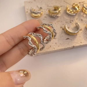 Detailansicht zweifarbiger Gold- und Silberohrringe in gedrehter C-Form in der Hand