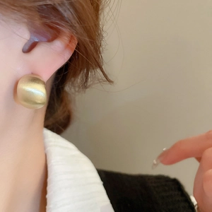 Close-up of a matte gold C-shaped earring on model ear showing smooth brushed texture