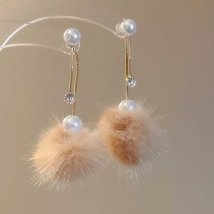 Close-up of pearl earrings with gold chains, zircon accents and soft brown pompom balls