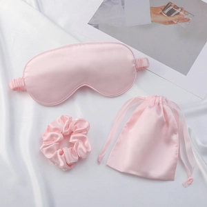 Flat lay of pink faux silk sleep set with an eye mask, scrunchie, and drawstring bag