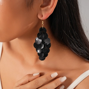 Macro shot of layered black shell discs on geometric tassel earrings worn by a model