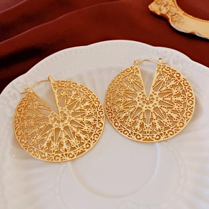 Détail macro de boucles d'oreilles filigranes dorées sur fond d'assiette en céramique