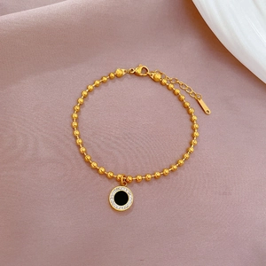 Detail of gold beaded bracelet featuring a round black pendant with shimmering diamonds