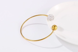 Détail d'un bracelet jonc doré en C avec une boule sertie de cristaux et une perle polie