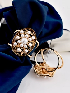 Detailed view of golden floral scarf ring with pearls on elegant dark blue fabric
